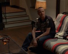 a man sitting on top of a couch in a living room next to a lamp