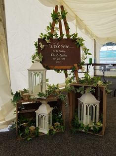 three white lanterns with greenery on them are sitting in front of a welcome sign