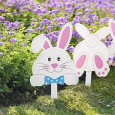 two wooden easter bunnies with bunny ears on them in the grass near purple flowers