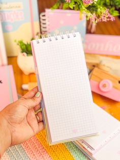 a person holding a notebook in their hand on top of a desk with other office supplies