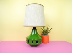 a green lamp sitting on top of a pink table next to a potted plant