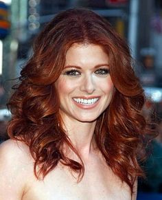 a woman with long red hair smiling at the camera and wearing a strapless dress