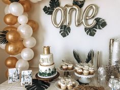 a table topped with cake and cupcakes next to an arch that says one