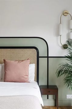 a bed with white sheets and pillows next to a potted plant on the wall