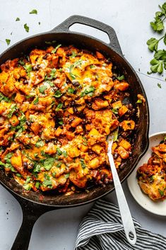 a skillet filled with chicken and vegetables on top of a white table next to a spoon