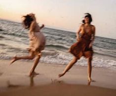 two women are running on the beach near the ocean at sunset or sunrise, one is wearing a brown dress