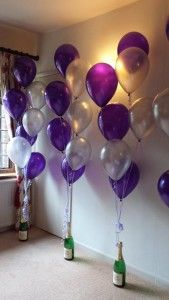 purple and white balloons floating in the air next to a window with curtains on it