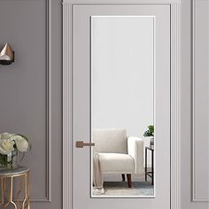 a white chair sitting in front of a mirror next to a table with flowers on it