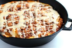 a skillet filled with cinnamon rolls covered in icing on top of a white table