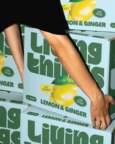 a woman's hand reaching into a box of lemon and ginger juice, which is stacked on top of each other