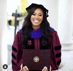 a woman in a graduation gown is holding a laptop computer and smiling at the camera