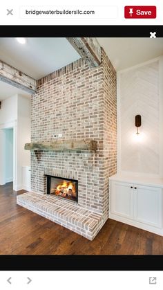 a brick fireplace in the middle of a room with wood flooring and white walls