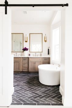 a large white bath tub sitting inside of a bathroom next to two sinks and mirrors