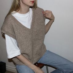 a woman sitting on top of a chair with her hand in her pocket and looking off to the side