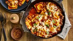 two pans filled with lasagna and sauce on top of a wooden table