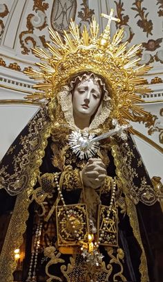 a statue of the virgin mary holding a cross in her hands and surrounded by gold decorations