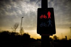 a pedestrian and bicycle crossing sign on a pole at dusk with clouds in the background