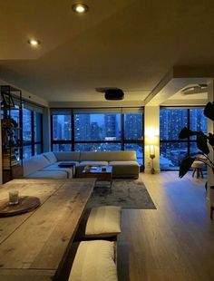 a living room filled with furniture and large windows next to a wooden floor covered table