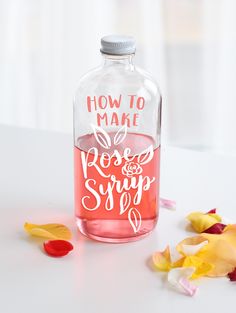 a clear bottle filled with rose syrup sitting on top of a table next to petals