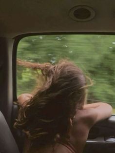 a woman sitting in the passenger seat of a car looking out the window at trees