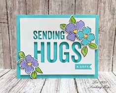 a card with flowers and the words sending hugs on it, sitting on a wooden surface