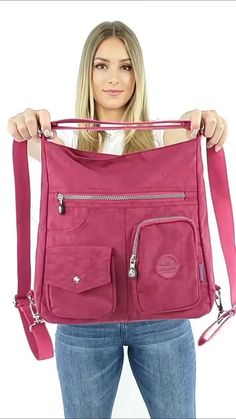 a woman holding up a pink purse with zippers on the front and side pockets