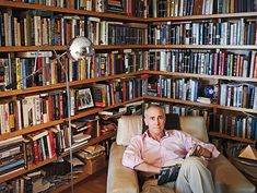 a man sitting on a chair in front of a bookshelf full of books