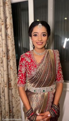 a woman in a red and gold sari standing next to a window with curtains