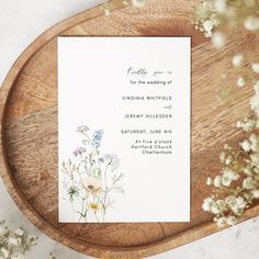 a wedding card with wildflowers on it sitting on top of a wooden platter