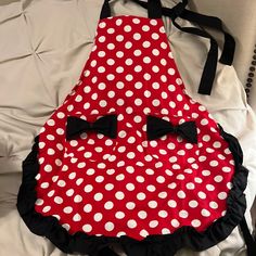 a red and white polka dot apron with black bow ties on the front, sitting on a bed