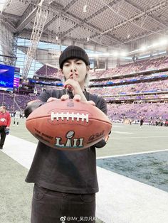 a person holding a football in front of an empty stadium filled with people and looking at the camera