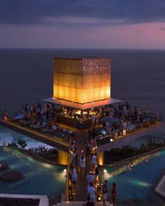 people are gathered at the top of a building overlooking the water and sky with lights on it