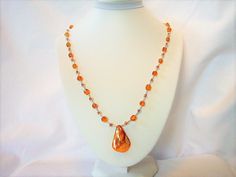 Ref: N025.    This necklace  has amber coloured glass beads, matching seed beads, silvery spacers and an amber coloured dyed shell pendant.  Length is 21 inches and has a sterling silver clasp.  It can be worn on either side one of which is smooth. Orange Baltic Amber Pendant Necklace, Orange Oval Beaded Necklaces As Gifts, Orange Oval Beaded Necklace For Gifting, Orange Oval Beaded Necklace For Gift, Amber Beaded Crystal Necklace For Gift, Elegant Orange Beaded Crystal Necklace, Amber Beaded Czech Glass Necklaces, Amber Beaded Necklace With Czech Glass, Orange Beaded Necklace With Polished Beads As Gift