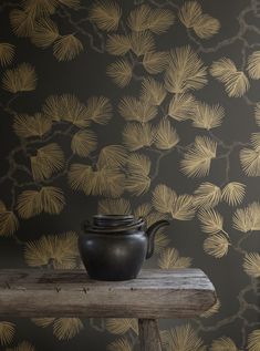 a black teapot sitting on top of a wooden table next to a wallpaper