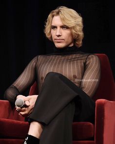 a woman sitting on top of a red chair in front of a black curtain holding a microphone