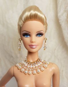 a barbie doll with blonde hair and blue eyes wearing a gold necklace, earrings and bracelet