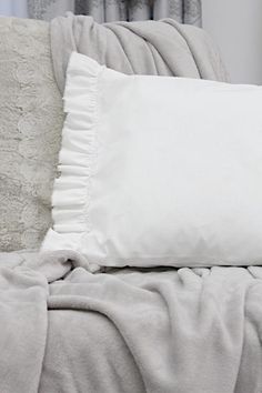 a white pillow sitting on top of a bed next to a gray and white blanket