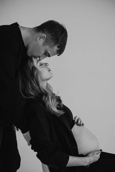 a man and woman standing next to each other in front of a white wall with their hands on the pregnant belly