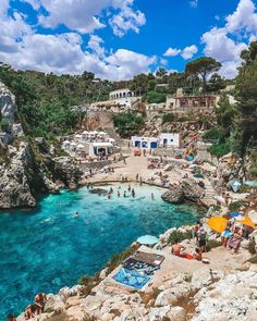 people are swimming in the blue water near some cliffs and houses on top of them