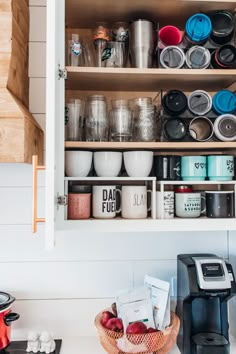 an open cabinet filled with lots of cups and bowls on top of a white counter