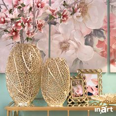 two vases sitting on top of a metal shelf next to pictures and flowers in front of a painting