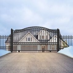 an iron gate and driveway leading to a house with snow on the ground in front of it