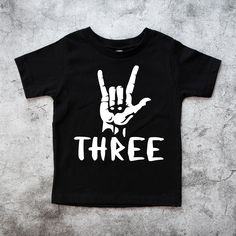 Three Rock on Birthday Shirt, 3rd Rock n Roll Birthday Tee, 3rd Birthday Boy outfit, Three year old Shirt, Born to Rock Theme Please read all the info before placing your order. The price you see is per shirt, please read the size chart in the last pictures of listings before placing your order. How to order a shirt: *Select the STYLE *Select the SIZE *Select the Quantity *Add Personalization *Add to cart *Go back and Repeat for each size (if you need more than one shirt) SHIRTS INFO: *Color: Gr Black Band Merch T-shirt For Birthday, Birthday Band Merch Tops With Short Sleeves, Short Sleeve Band Merch Tops For Birthday, Band Merch Tops For Birthday With Short Sleeves, Black Summer Shirt For Birthday, Black Shirt For Summer Birthday, 3 Year Birthday Theme Boy, Rock N Roll Birthday, 3rd Birthday Boy