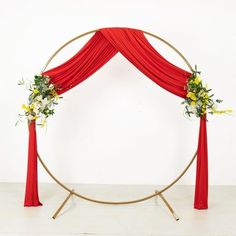 an arch with red drapes and flowers on the top is decorated with gold hoop