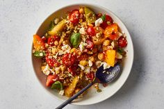 a white bowl filled with lots of food on top of a table next to a spoon