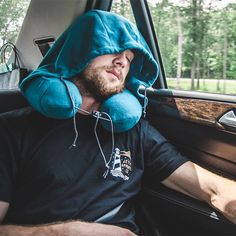 a man in a car with a blue pillow on his head and hood over his face