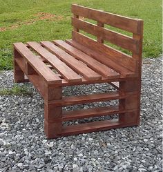 a wooden bench sitting on top of a gravel covered ground next to a green field