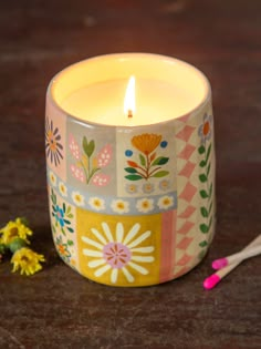 a lit candle sitting on top of a table next to some flowers and spoons