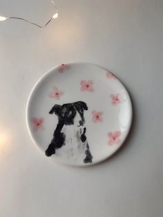 a plate with a black and white dog sitting on it's side next to a string of lights