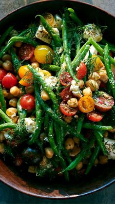 a bowl filled with green beans, tomatoes and chickpeas on top of a table